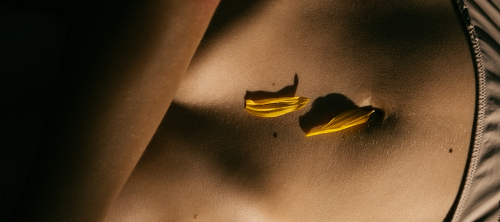 Torso femenino con pétalos amarillos en luz contrastada evocando conexión corporal en endometriosis síntomas diagnóstico